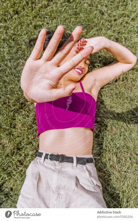Asiatische Frau spielerisch auf Gras liegend Hand Deckung Gesicht Lügen nach unten sonnig Tag im Freien Erholung Freude Sommer grün Natur Lächeln pulsierend