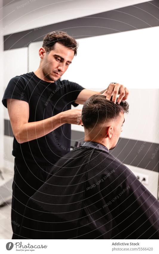 Junger Friseur bei der Arbeit in einem Friseursalon. Behaarung Schere Kamm Stil Salon weiß Mann fokussiert Kleidung schwarz T-Shirt Haarpflege Präzision Pflege