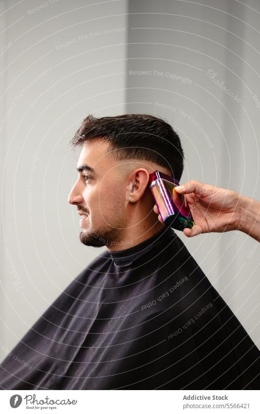 Ein Friseur benutzt eine elektrische Haarschneidemaschine, um einem männlichen Kunden die Haare zu schneiden. Schermaschine Klient entgittern Behaarung Seite