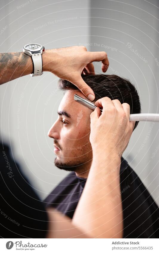 Friseur, der die Haare eines Kunden mit einem Rasiermesser schneidet. Rasierer Haarschnitt Formgebung Klinge Salon männlich Klient Fokus Pflege Präzision