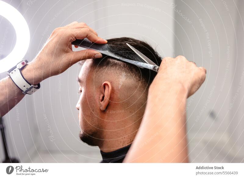 Friseur, der die Haare mit Kamm und Schere in einem Friseursalon stylt. Behaarung geschnitten Rücken Kopf Licht Salon weiß Wand kreisrund Stil Nahaufnahme Hand