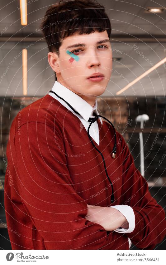 Trendiges junges männliches Modell mit Augenfarbe und um den Hals gebundenem Verbindungskabel in einer hellen Umgebung. Konzept Arbeit Gen-Z Gesicht Farbe
