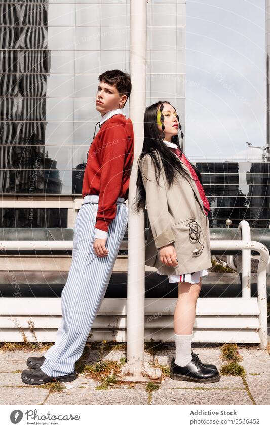 Modeporträt eines Gen-Z-Duos mit Kabeln vor einem modernen städtischen Gebäude. duo im Freien Arbeit Pose Stil männlich Frau urban lässig Mantel Pullover Schuhe