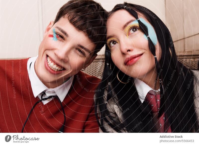Gen-Z-Duo mit lebhaftem Gesichts-Make-up in Nahaufnahme. Jugend pulsierend duo Lächeln Pose im Innenbereich Hintergrund Gesichtsbehandlung Kunst männlich Frau