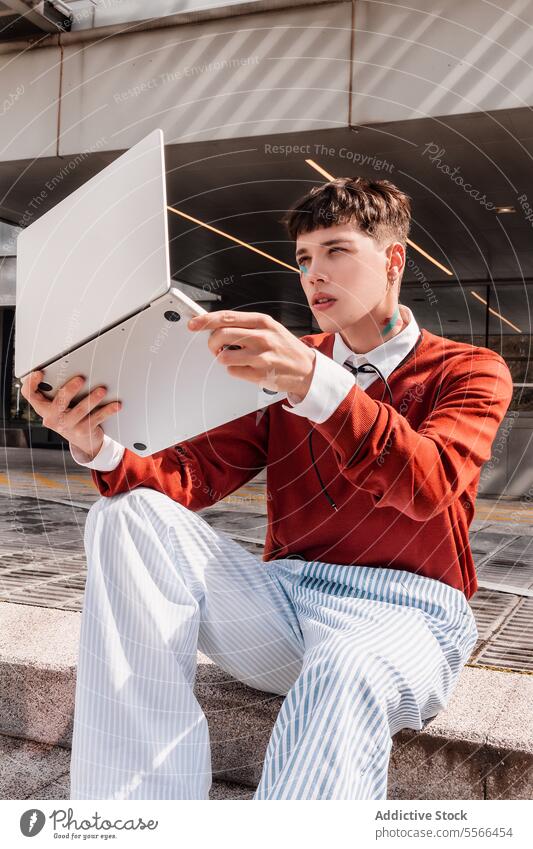 Stadt junge gen-z Mann hebt einen Laptop mit seiner Hand in der Mode arbeiten Konzept. Gen-Z Arbeit Technik & Technologie männlich im Freien Architektur Stil
