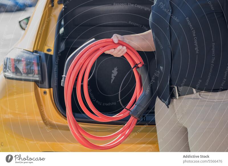 Anonyme Person mit Kabel, die ein Elektroauto aufladen will rot elektrisch PKW gelb Fahrzeug Ladegerät Vorbereitung Hand Kofferraum Stecker Zwischenstück