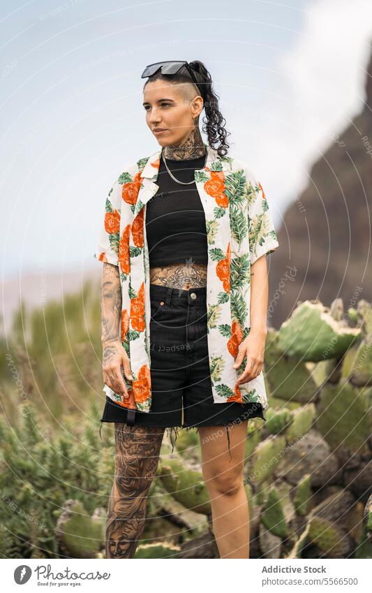 Lächelnde tätowierte Frau auf unscharfem Kaktus stehend stylisch Natur genießend Tattoo Stehen attraktiv jung Mode hübsch Stil cool Schönheit trendy lässig
