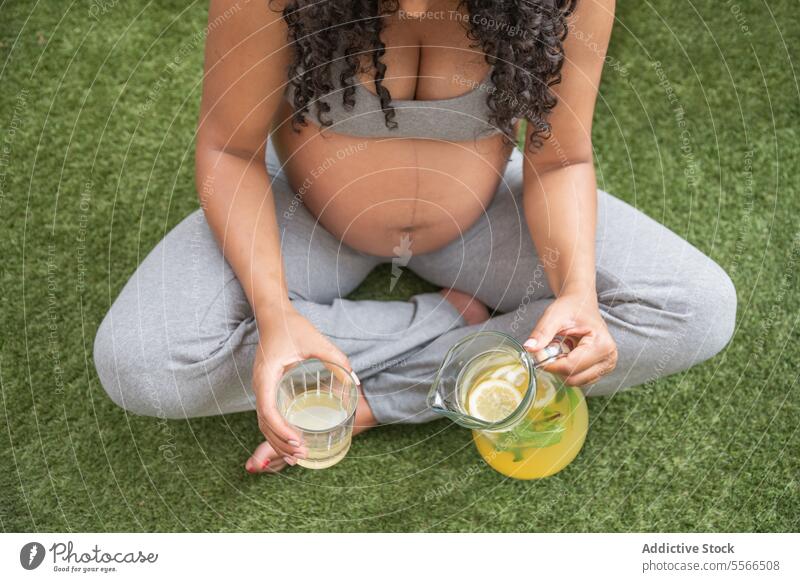 Schwangere Frau genießt ein gesundes Getränk im Freien Schwangerschaft trinken Gras Gesundheit Kannen Glas Gießen Erfrischung Sitzen Freizeit Erholung Natur