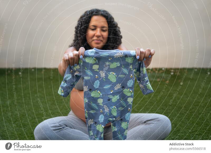 Werdende Mutter präsentiert Baby-Strampler im Freien Schwangerschaft erwartungsvoll Natur Muster blau Freude Vorfreude Bekleidung Garten Frau Mutterschaft