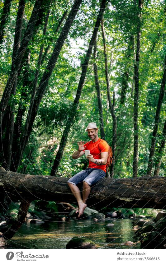 Mann mit Hut und rotem T-Shirt im Gespräch mit Smartphone inmitten der Waldstille Wanderer Totholz reden Ruhe Baum grün sitzend Anruf Technik & Technologie