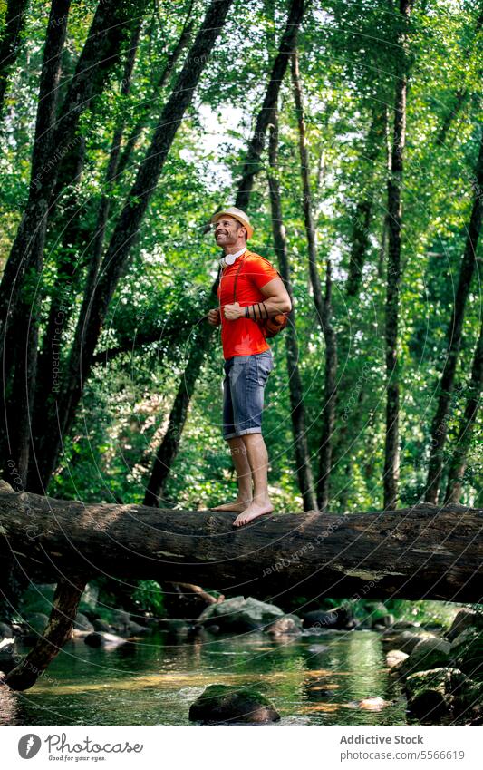 Wanderer lächelnder Mann auf einem umgefallenen Baumstamm im üppigen grünen Wald. stehen Totholz selbstbewusst Reisender Glück Blick Bewältigung Natur Wasser