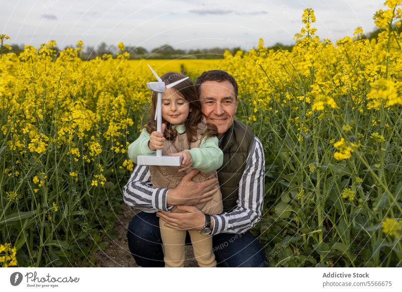 Vater-Tochter-Umarmung mit Windmühlen-Spielzeug auf einem Feld. Umarmen Blume gelb binden Liebe Familie Natur Miniatur Freude Lächeln Kind im Freien Wiese