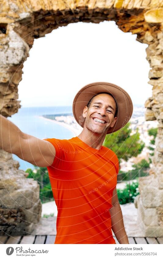 Ein glücklicher Reisender macht ein Selfie vor dem Hintergrund der Küste von Barcelona. Mann Telefon Fotokamera Smartphone Freude Blick Bogen orange Hemd