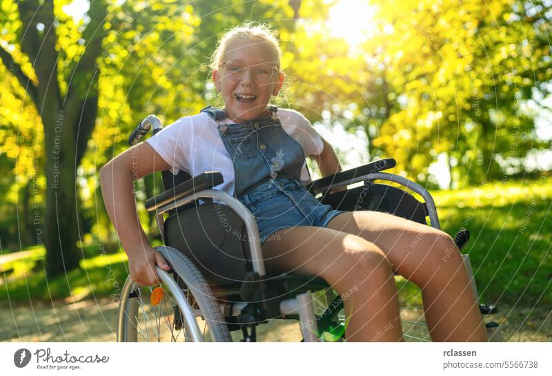 Glückliches junges behindertes blondes Mädchen sitzt im Rollstuhl während eines Spaziergangs im Park, Teenager Behinderung Konzeptbild Rad Stuhl Lähmung Pflege