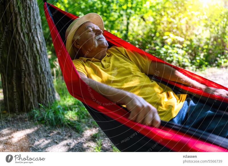 Älterer Mann mit Strohhut genießt ein friedliches Nickerchen in einer Hängematte im Park Großvater älterer Herr Erholung Natur Mittagsschlaf Wald im Freien Ruhe