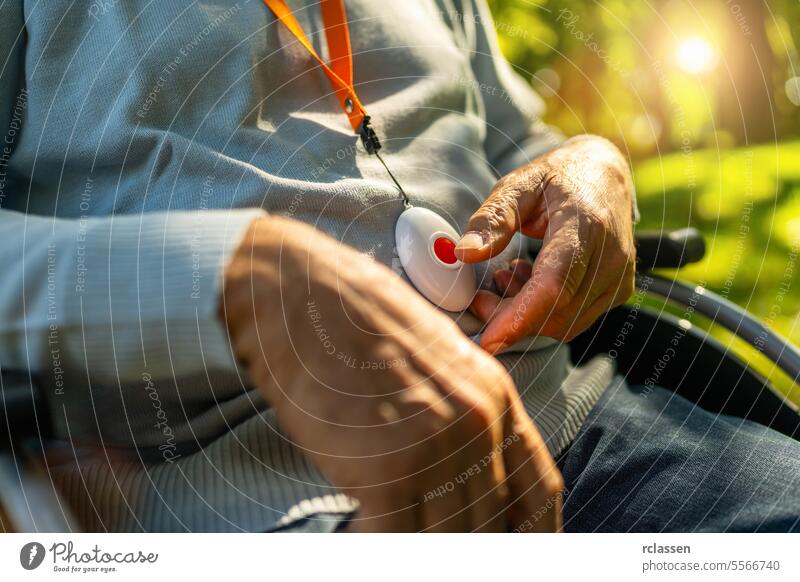Senior Mann drückt Alarmknopf in einem Rollstuhl draußen in einem Park, Nahaufnahme. Notrufsystem Konzeptbild. Hand medizinisch Alarmanlage Alarmtaste älter
