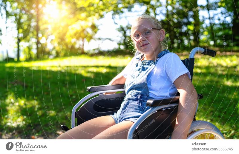Glückliches junges behindertes blondes Mädchen sitzt im Rollstuhl während eines Spaziergangs im Park, junger behinderter Teenager im Invalidenwagen oder Rollstuhl, junges Behinderungskonzeptbild