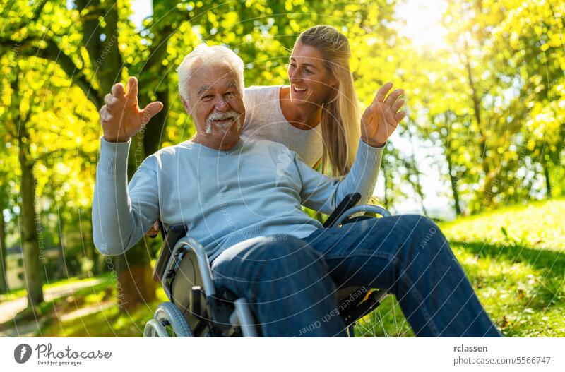 Glückliche Tochter, die ihren Großvater im Pflegeheim besucht und mit ihm im Rollstuhl im Park spazieren geht. Fröhliche Momente Konzept Bild Krankenpfleger