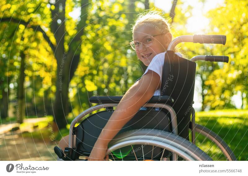 Lächelndes junges behindertes blondes Mädchen sitzt im Rollstuhl während eines Spaziergangs im Park, Teenager Behinderung Konzeptbild Glück Rad Stuhl Lähmung
