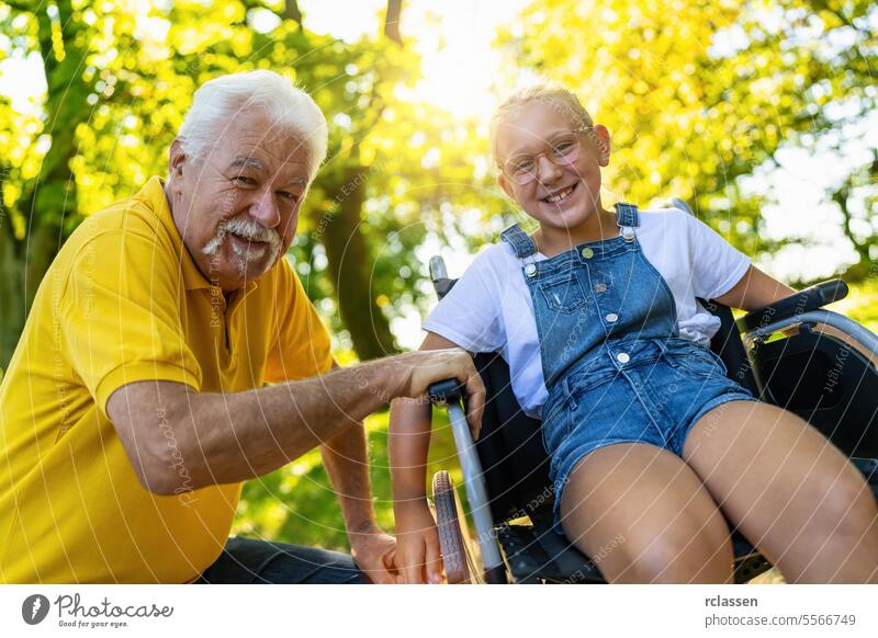 Glücklicher Großvater und Enkelin in wheelcahir bei einem Spaziergang im Park im Sommer Frau Mädchen Rollstuhl Bonden Familie Natur Lächeln Fröhlichkeit