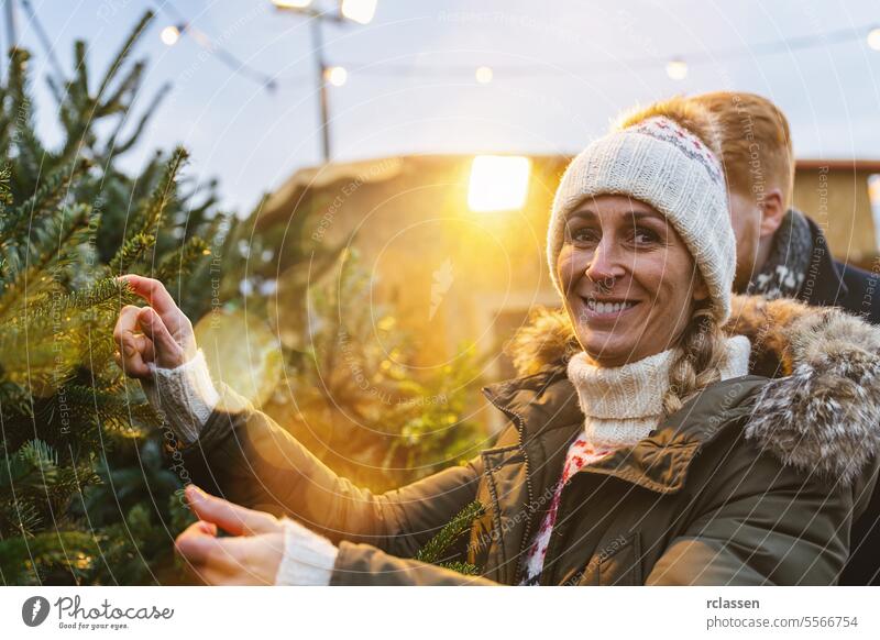 Glückliche Frau und ihr Freund wollen einen Weihnachtsbaum kaufen und schauen in die Kamera Rotschopf Tradition Wahl Lächeln Mann Liebespaar Kauf Bauernhof