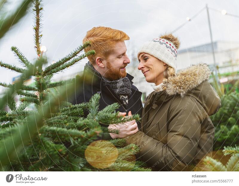 Verliebtes Paar auf einem Weihnachtsbaummarkt betrachten Kuss Familie Glück Rotschopf Tradition Wahl Lächeln Mann Liebespaar Kauf Bauernhof Kiefer Norwegen