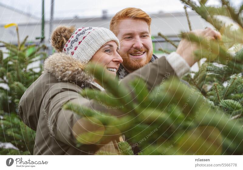 Glückliches Paar sucht Weihnachtsbaum auf dem Weihnachtsmarkt aus überrascht Familie skeptisch Rotschopf Tradition Wahl Lächeln Mann Liebespaar Kauf Bauernhof