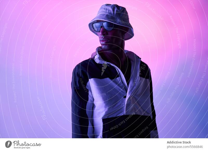 Stilvoller schwarzer Mann mit Hut und Brille posiert im leuchtenden Studio jung stylisch Outfit Model Studioaufnahme Sonnenbrille sorgenfrei posierend Stehen