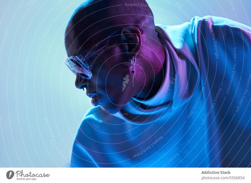 Stilvoller schwarzer junger Mann mit Sonnenbrille im Studio ernst kahl Ohrringe herabsehend Studioaufnahme modern leuchten Licht Seitenansicht selbstbewusst