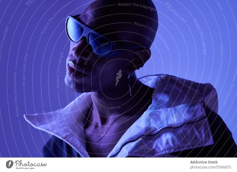 Männliches Modell mit Glatze und Sonnenbrille posiert auf blauem Hintergrund Mann jung stylisch kahl selbstbewusst Freizeitkleidung Blick posierend Piercing