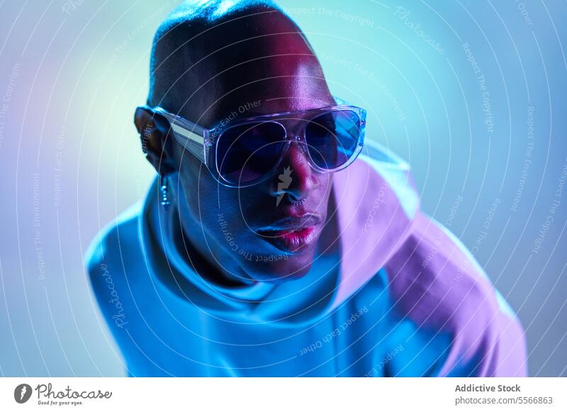 Stilvoller schwarzer junger Mann mit Sonnenbrille im Studio ernst kahl Ohrringe Studioaufnahme modern leuchten Licht Seitenansicht selbstbewusst Piercing Model