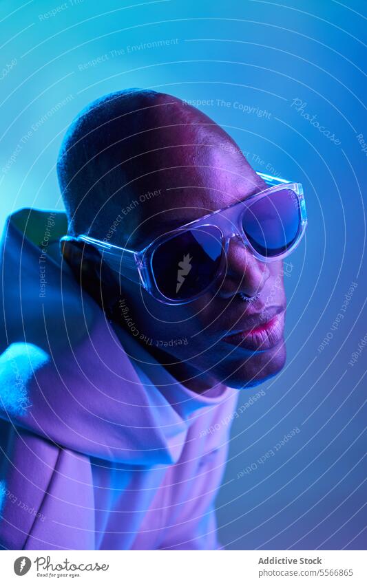 Stilvoller schwarzer junger Mann mit Sonnenbrille im Studio ernst kahl Ohrringe Studioaufnahme modern leuchten Licht Seitenansicht selbstbewusst Piercing Model