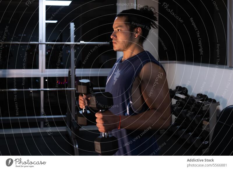 Seriöse Person bei der Ausübung ihrer Tätigkeit Mann Kurzhantel Fitnessstudio Großstadt Licht Nacht Fenster Stärke Fokus Muskel Training heben