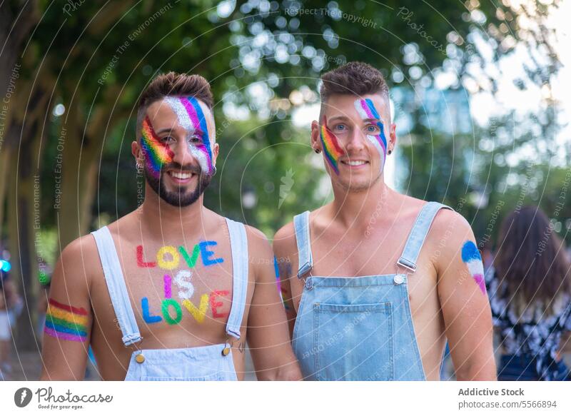 Bemalte Männer feiern den LGBT-Stolz im Freien Mann Farbe Lächeln Jeansstoff Gesicht Feier farbenfroh Straße Stadtfest Liebe lgbtq Einheit Gleichstellung Freude