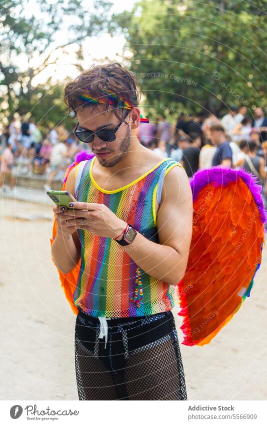 Mann telefoniert bei der Pride-Feier in einem Park jung Zubehör Stirnband Tank Mobile Telefon Stadtfest Sonnenbrille Feder Flügel Menschen Veranstaltung