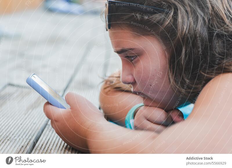 Mädchen, das auf einem Holzdeck auf ein Smartphone schaut. Schiffsdeck blau Top Fokus Ansicht Inhalt liegen Bildschirm digital Gerät Technik & Technologie jung