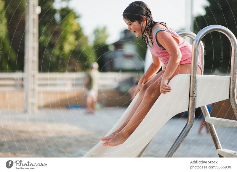 Ein Mädchen genießt die Rutsche im Freibad. Sliden Pool Badeanzug gestreift im Freien Spaß Sommer Sonne Freude spielen weiß Beckenrand Tag Lachen Wasser