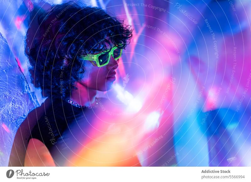 Nachdenklicher lateinamerikanischer Mann mit Neonröhren unter Lichtern Latein neonfarbig Porträt Sonnenbrille grün krause Haare beschaulich pulsierend Farbtöne