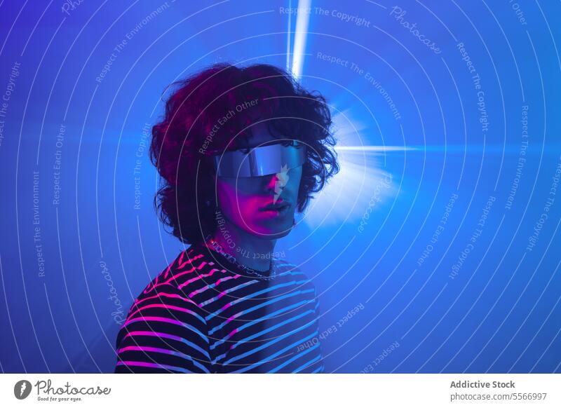 Lateinamerikanischer Mann mit futuristischer Brille, die in blaues Licht getaucht ist lockig Behaarung gestreift virtuell Realität VR Hemd Metaversum purpur
