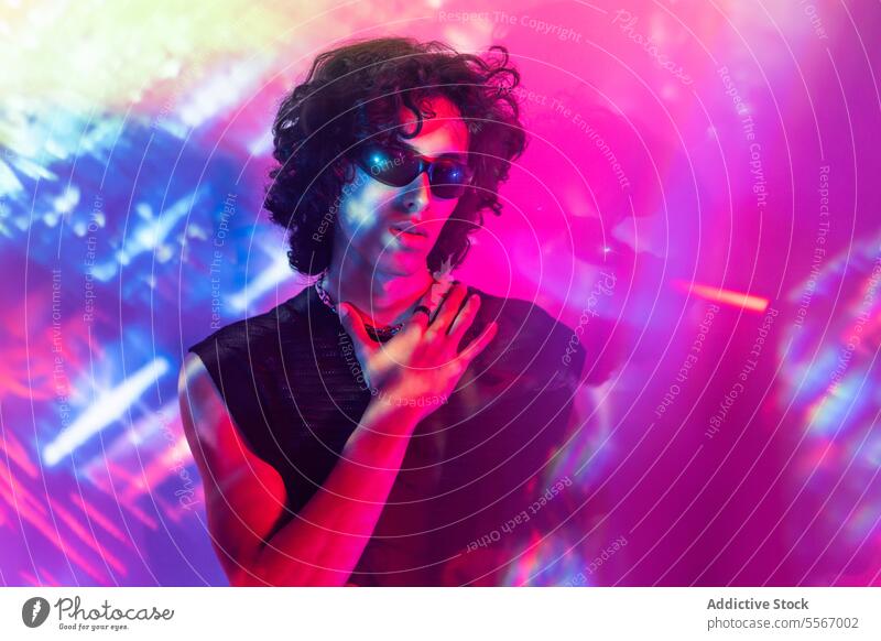 Lateinamerikanischer Mann mit Sonnenbrille inmitten eines leuchtenden Neonspektakels neonfarbig farbenfroh krause Haare strahlend Pose Lichter Spektakel