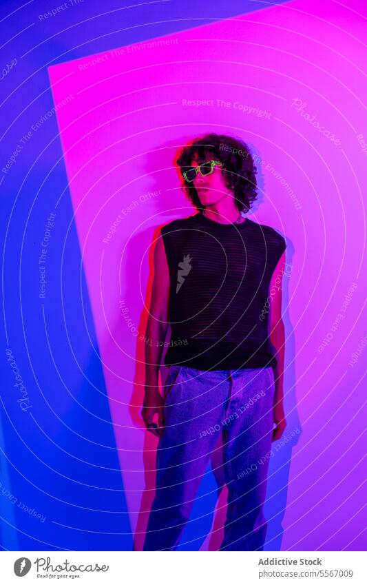 Lockenhaariger Latino im Netzpanzer mit Neon-Hintergrund Mann Latein lockig Behaarung Stil neonfarbig blau rosa Sonnenbrille ineinander greifen Tank Top Mode