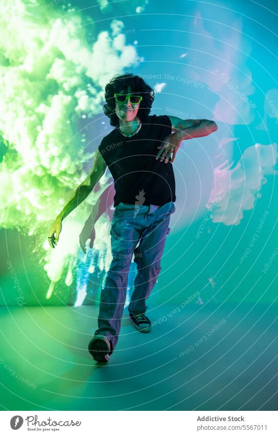Dynamischer Sprung eines lateinamerikanischen Mannes inmitten einer Neonwolken-Atmosphäre Latein neonfarbig grün Cloud Sonnenbrille Bewegung Energie Jeanshose