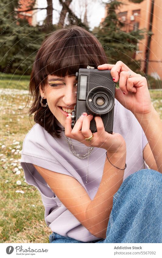Lächelnde Frau beim Fotografieren mit einer Retro-Kamera im Stadtpark fotografieren Fotoapparat altehrwürdig Tourist heiter Glück Natur positiv jung brünett