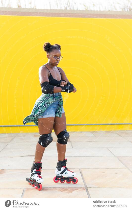 Junge Frau, die beim Rollerskaten im Skatepark ihre Handgeräte befestigt Schlittschuhlaufen befestigen Ausrüstung lässig Wand gelb Skateplatz Sport üben