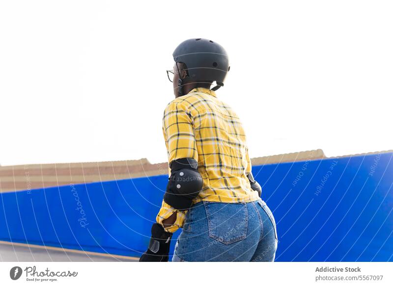 Frau in Schutzkleidung Rollschuhlaufen im Skatepark bei klarem Himmel Schlittschuhlaufen Schutzhelm Hemd Ausrüstung blau Wand sonnig lässig Plaid Skateplatz