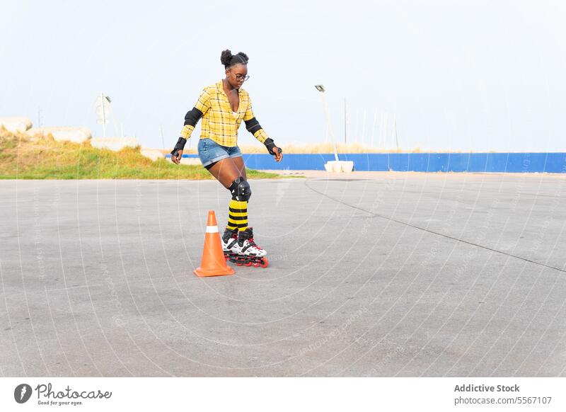 Frau, die auf Rollschuhen durch einen Kegel fährt, während sie auf einer Eisbahn im Skatepark übt Rolle Schlittschuhlaufen Zapfen üben lernen Schutz lässig