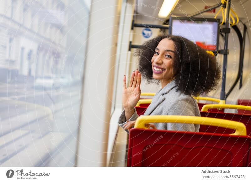 Junge Afro-Frau winkt im Bus lockig Behaarung Fenster Reflexion & Spiegelung Großstadt Transport Freude Sitz rot Arbeitsweg Öffentlich reisen urban Reise Mantel
