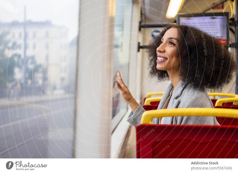 Glückliche afroamerikanische Frau schaut durch das Fenster, während sie auf einem Bussitz sitzt lockig Behaarung Reflexion & Spiegelung Großstadt Transport