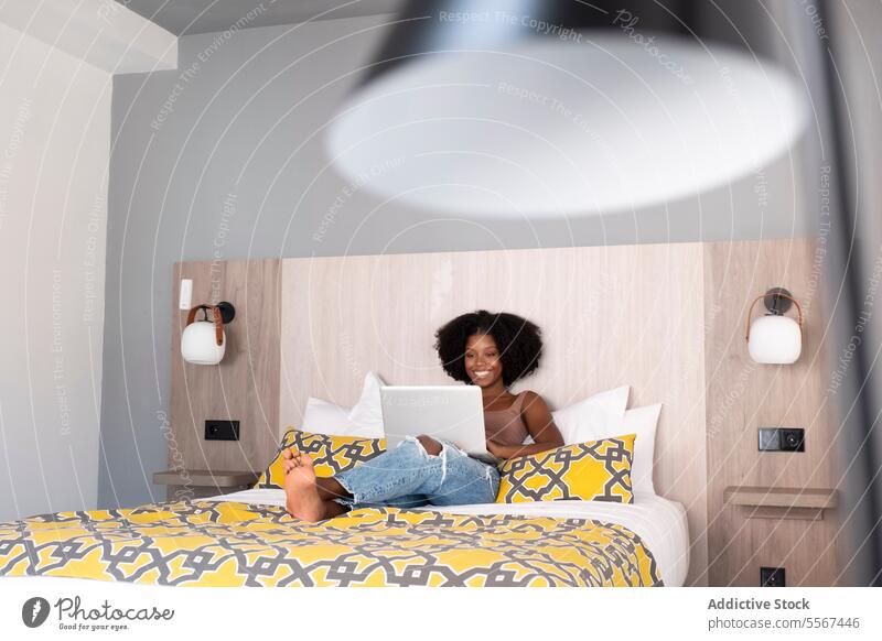 Schwarze Frau in moderner Entspannung lockig Laptop Bett Dekor heiter Arbeit sich[Akk] entspannen ethnisch Technik & Technologie im Innenbereich Panel Wand