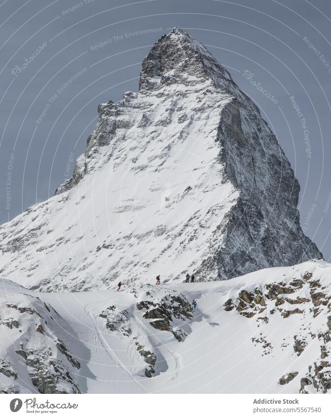 Skifahrer auf dem Bergrücken neben einem majestätischen, schneebedeckten Berggipfel anonym schlendernd verschneite Kamm Schnee unkenntlich Berge u. Gebirge